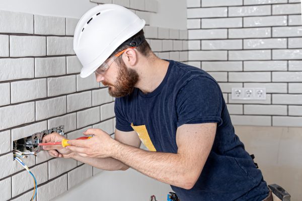 Electrician construction worker with a beard in overalls during the installation of sockets. Home renovation concept.